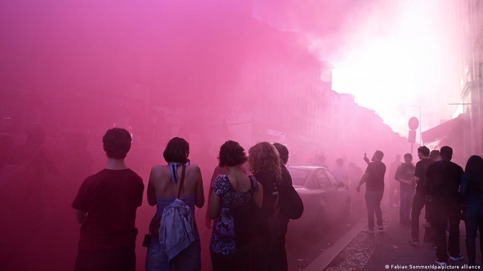 Menschen stehen auf der Straße und rosa Rauch erfüllt die Luft