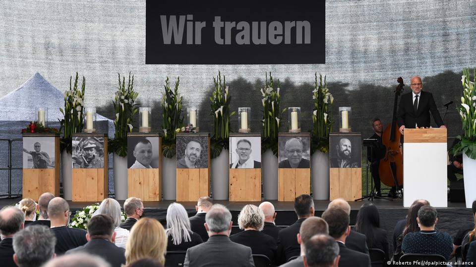 Menschen sitzen vor Schwarz-Weiß-Fotos der sieben Opfer