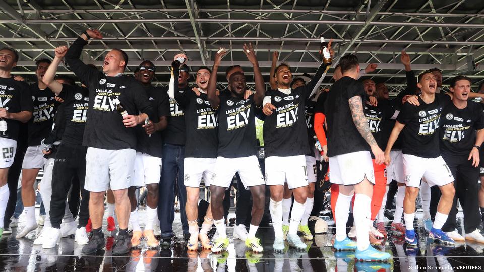 Fußballspieler in schwarzen T-Shirts und weißen Shorts tanzen auf einer Bühne