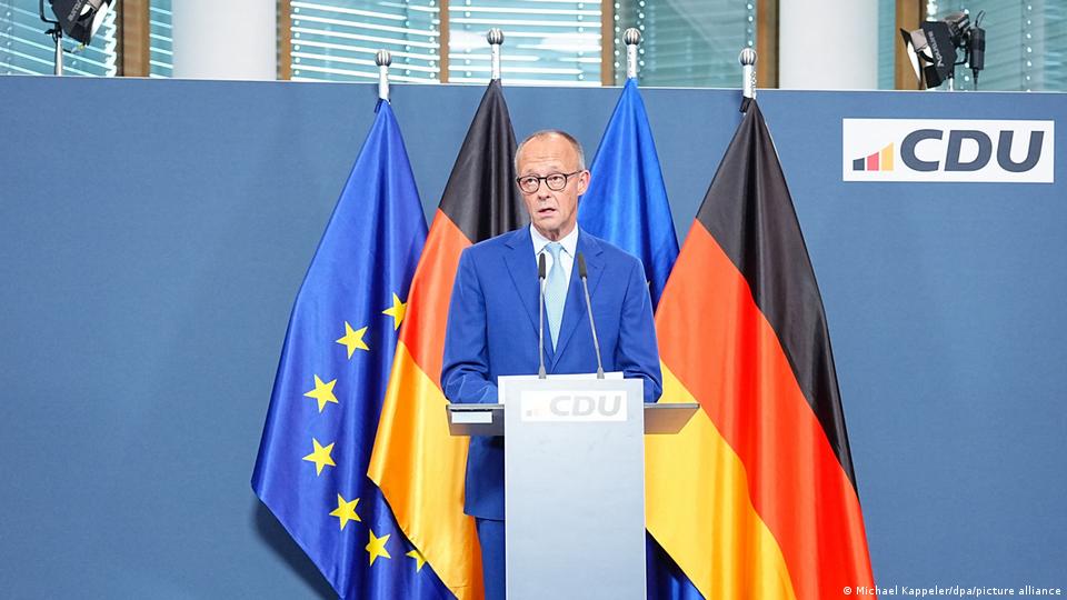 Friedrich Merz steht an einem Rednerpult mit der Aufschrift „CDU“, vor EU- und Deutschlandfahnen und dem CDU-Logo