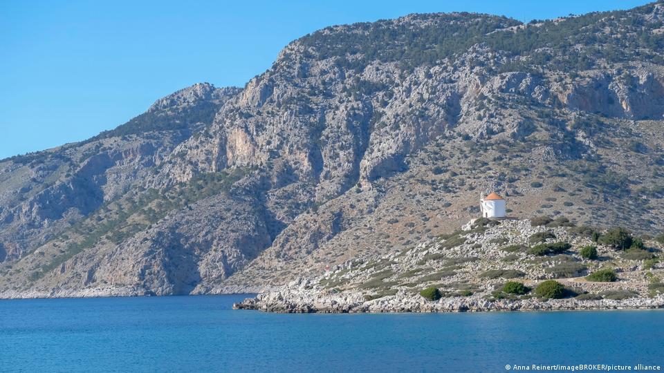 Auf einem Felsvorsprung vor den schroffen Bergen auf Symi ist eine alte Windmühle zu sehen