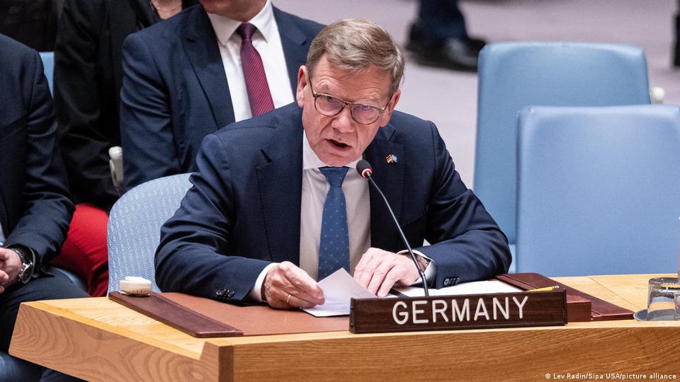 Johann Wadephul, ein Mann mit Brille, der vor einem Mikrofon sitzt, mit der Aufschrift „Deutschland“ auf einer Holzlatte vor ihm