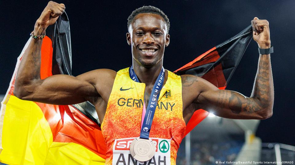 Owen Ansah hält eine Deutschlandfahne mit erhobenen Armen und eine Bronzemedaille um den Hals