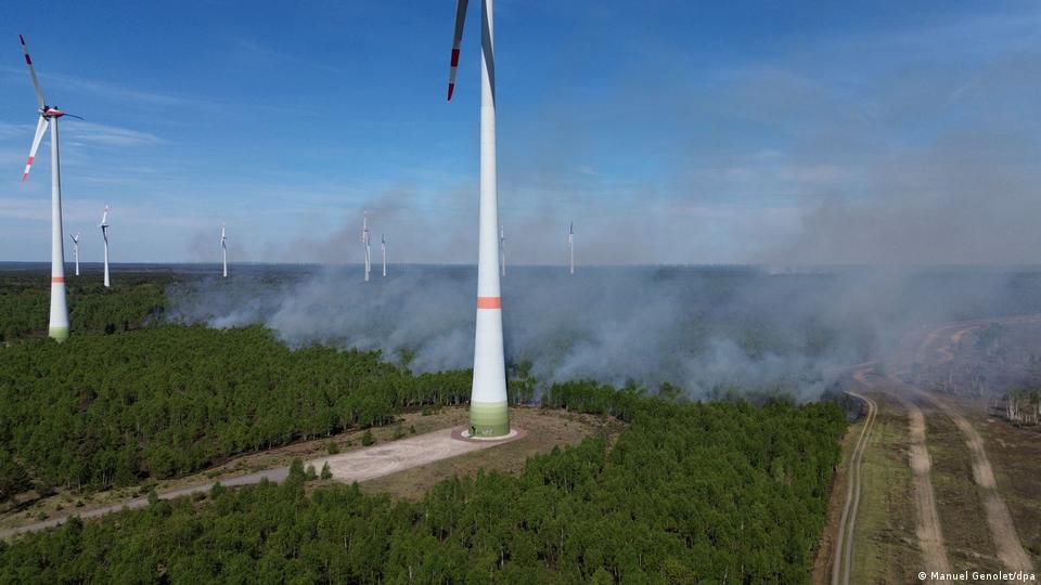  Mehrere Windkraftanlagen stehen in der Nähe eines Waldgebietes, das in Flammen steht